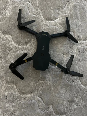 Emotion Drone - Emotion Drone med fjärrkontroll, kompakt och vikbar design. Utrustad med kamera för flygfotografering. Skick: begagnad, mindre slitage synligt på propellrar och armar. Perfekt för nybörjare som vill testa drönarflygning och ta bilder från luften.