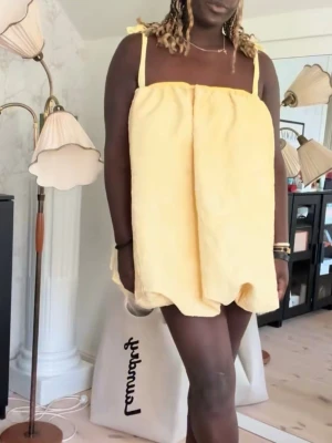 Gul balong kortklänning med volang - Superfin gul kortklänning från ASOS med breda axelband som knyts upptill. Klänningen har en unik volangformad siluett och är tillverkad i ett blommigt mönstrat tyg med struktur. Perfekt för dig som gillar statement-plagg och vill sticka ut med en lekfull look.