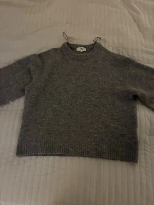 Grå stickad tröja från Gina Tricot -  grå stickad tröja från Gina Tricot!Tröjan har rund hals, ribbade muddar vid ärmslut och nederkant samt långärmad passform. Perfekt för kyliga dagar och kan användas året om.