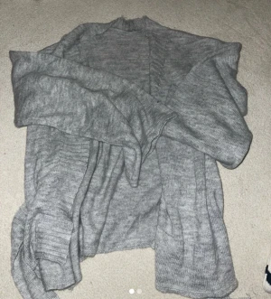 Grå stickad kofta med bälte - Säljer en grå stickad kofta med bälte i midjan. Koftan har långärmade ärmar och är i mjukt material som passar perfekt för kyliga dagar. Enkel och stilren design som är lätt att matcha med olika outfits.