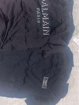 Balmain paris t-shirt - Säljer en svart t-shirt från Balmain Paris med tryckt logga framtill. T-shirten har rund hals och korta ärmar, perfekt för dig som gillar stilrena designer och exklusiva märken. Materialet känns mjukt och skönt mot huden.    400kr st, 700kr för båda