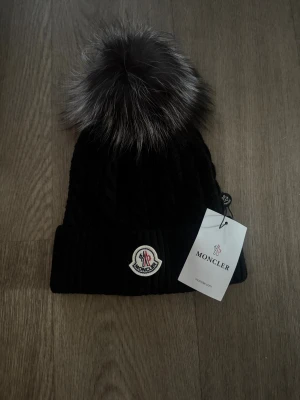 Svart  mössa med pälsboll - Svart  mössa med  fluffig pälsboll på toppen