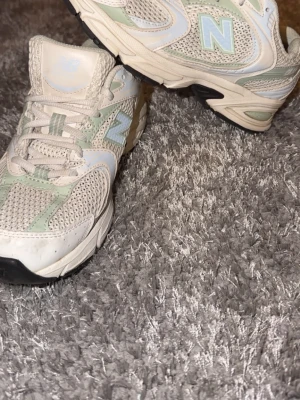New Balance sneakers i beige och mint - Säljer ett par snygga New Balance sneakers i storlek 38. Skorna har en beige mesh-överdel med mintgröna och vita detaljer, samt en rund tå och platt sula. Klassisk N-logga på sidan och snörning framtill. Perfekta för dig som gillar sportig stil.