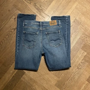 Replay Grover blå jeans straight fit - Säljer ett par klassiska blå jeans från Replay, modell Grover. Jeansen har raka ben, fem fickor och snygga detaljer på bakfickorna. De är tillverkade i slitstarkt denim och har en normal passform med knapp och dragkedja framtill. Hål i vänstra ficka