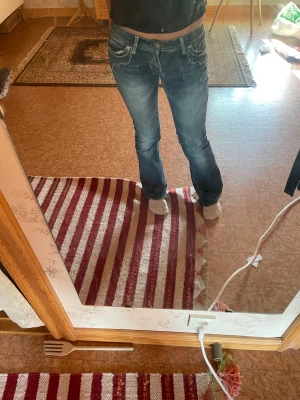 Blå bootcut jeans från Guess - Säljer ett par blå jeans med mjukare tyg från Guess med bootcut-snitt och låg midja. Jeansen har tydliga vita kontrastsömmar, klassiska fem fickor och snygga detaljer på bakfickorna. Materialet är jeans med slitningar och broderade detaljer. Perfekt för dig som gillar jeans från 20talet. Jag har spretat upp jeansen längst ner på benet. Säljer eftersom dom är för små.