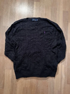 Svart stickad tröja Polo Ralph Lauren - Snygg svart kabelstickad tröja från Polo Ralph Lauren med lila logotyp. Perfekt för kyliga kvällar eller som ett stilrent lagerplagg. Riktigt skön och klassisk design. Passar cirka 183 🙌  Skick 9/10 ✅ Nypris ca 1700.  Skickar inom 24 timmar med tanke på jul snart 🚚🎄