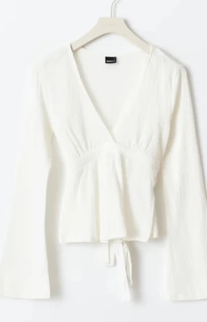Vit omlottopp från Gina Tricot - Säljer en vit omlottopp från Gina Tricot i storlek S. Toppen har lång ärm, v-ringad hals och knyt i midjan. Materialet är lätt strukturerat och känns mjukt mot huden. Perfekt att styla med jeans eller kjol för en fräsch look.