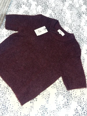 Vinröd stickad topp från Gina Tricot  - Säljer en vinröd stickad topp från Gina Tricot med korta ärmar och rund hals. Mjuk och fluffig känsla, perfekt för lager på lager. Stilren design utan detaljer, passar till jeans eller kjol. Lappen sitter kvar.