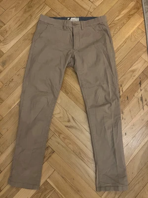Beige chinos slim fit från Dressmann - Säljer ett par beige chinos från Dressmann i slim fit-modell. Byxorna har klassisk design med fickor fram och bak, bälteshällor och knappstängning. Materialet är 98% bomull och 2% elastan vilket gör dem både mjuka och lite stretchiga.