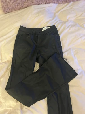 Svarta bootcut jeans från Vero Moda - Svarta jeans från Vero Moda med bootcut-snitt och klassisk femficksdesign. Byxorna är tillverkade i ett jeansmaterial och har bälteshällor samt knapp och dragkedja framtill. Perfekta för dig som gillar en tidlös look med lite extra vidd vid benslutet.