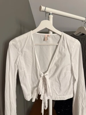 Vit omlottopp med knyt från Nelly - Säljer en vit omlottopp från Nelly i storlek 34. Toppen har lång ärm, djup v-ringning och knyt framtill. Aldrig andvänd 