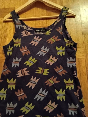 Mönstrad linnetopp från Gudrun Sjöden - Säljer en cool topp från Gudrun Sjöden med unikt mönster i grönt, blått och brunt på mörkblå botten. Toppen är ärmlös och har rund halsringning, perfekt för dig som gillar färg och grafiska prints. Färgen är lite mer matt egentligen den blev väldigt klarblå på bilden. 