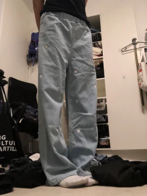Ljusblå wide jeans med hjärtan - Säljer ett par ljusblå jeans med bred passform och små broderade hjärtan över hela byxorna. De har resår i midjan för extra komfort och är perfekta för en avslappnad och trendig look.