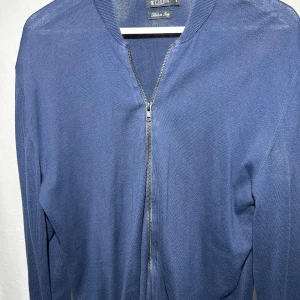 Marinblå kofta från Tiger Of Sweden - Snygg marinblå cardigan jacka från Tiger med stilren design och hel dragkedja framtill. Jackan är stickad i ett mjukt material och har ribbade muddar vid hals och ärmslut. Perfekt för dig som gillar enkel och clean stil.