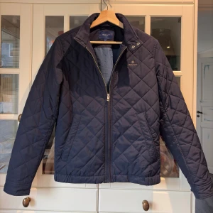 Mörkblå quiltad jacka Gant - Säljer nu en stilren jacka från Gant. Den är quiltad och endast änvända en halv säsong. Jackan är i nyskick och det finns inga märken på slitage eller liknande! Den är även i storlek xs och säljer nu pågrund av att den inte passar längre. Jackan är 100% äkta och är köpt för 2500kr. Knapparna på sista bild hänger med vid köp. Hör av er vid mer frågor/ Mio :)