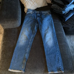 Replay Thad blå jeans straight fit - Blå jeans från Replay, modell Thad, med klassisk femficksdesign och raka ben. Jeansen har snygga slitningar och kontrastsömmar, samt Replay-logga på fickan. Passformen är straight och materialet är robust denim i bomull.