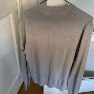 Grå stickad tröja från Filippa K - Snygg grå stickad tröja från Filippa K med rund hals och ribbade muddar. Enkel och stilren design som funkar till jeans eller chinos. Långärmad och mjuk i materialet, perfekt för dig som gillar minimalistisk stil.