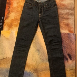 Nudie Jeans Grim Tim Dry Navy - Säljer ett par mörkblå Nudie Jeans Grim Tim i modellen Dry Navy. Jeansen är tillverkade i Dry navy material så att den formar sig efter din passform och tvättningar. Klassisk femficksdesign, raka ben och snygga kontrastsömmar. Perfekta för dig som gillar stilrena jeans med schysst passform.