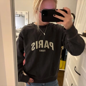 Svart sweatshirt med Paris-tryck XS - Cool svart sweatshirt från H&M i storlek XS med stort vitt tryck 'PARIS FRANCE' på bröstet. Tröjan har rund hals, ribbade muddar och en relaxed passform. Perfekt för dig som gillar streetstyle och vill ha en enkel men snygg look.