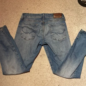 Slim Glenn jeans från Jack & Jones - Snygga ljusblå jeans från Jack & Jones, modell Slim Glenn. Jeansen har klassisk femficksdesign, smal passform och är tillverkade i mjukt denimtyg. Perfekt för dig som gillar en modern och stilren look med slim fit.