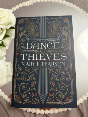 Dance of Thieves - En snygg och mystisk bok med elegant omslag, perfekt för dig som gillar spänning och äventyr. Skriven av Mary E. Pearson, känd för sina populära ungdomsromaner. Passar dig som vill ha något fängslande och episkt i bokhyllan.