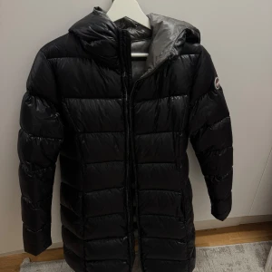  Vinterjacka från Colmar - Säljer en svart, lång dunjacka från Colmar med huva i storlek M  . Jackan har dragkedja framtill och ett snyggt Colmar-märke på ärmen. Insidan är grå och materialet är glansigt och lätt, perfekt för kalla dagar. Passformen är normal och jackan är långärmad. Säljer pga att den blivit för stor för mig och pris kan diskuteras! 