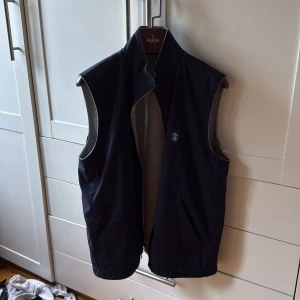 Brunello Cucinelli väst  - Vändbar väst från Brunello Cucinelli med ena sidan i svart och andra i ljusgrått. Västen har ståkrage, tvåvägsdragkedja med logodetaljer och två fickor på varje sida. Vattentät på ena sidan. Nypris ligger runt 20-25 tusen. Den är precis som från butik mer eller mindre helt ny. Storlek L/M. 