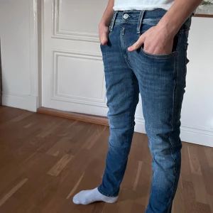 Replay Ambass - Snygga blå jeans med slim passform och klassisk femficksdesign. Jeansen har normal midja, raka ben och diskreta slitningar framtill. Materialet är mjukt denim som sitter skönt och följer kroppen. Perfekta för en avslappnad och stilren look.