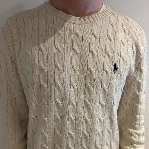 Beige kabelstickad tröja Polo Ralph Lauren - Hej 👋 Jag säljer min Kabelstickad beige tröja från Polo Ralph Lauren med klassisk rund hals och broderad marinblå logga på bröstet. Tröjan är i mjuk bomull och har långärmad passform med ribbade muddar. Perfekt för dig som gillar stilrena och tidlösa plagg. Hör av dig vid frågor och funderingar✅💬
