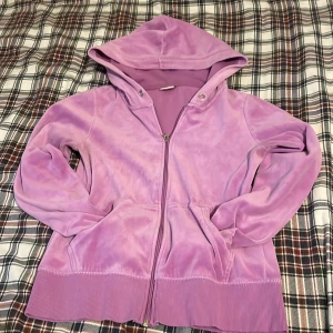 Ljuslila hoodie med strass från C - Säljer en mjuk och lyxig ljuslila hoodie från C i storlek XS. Tröjan har huva, dragkedja och fickor framtill. Baksidan är dekorerad med strass och texten 'LIVIN' THE DREAM' som ger extra bling. Materialet är sammet och ribbade muddar vid ärmslut och nederkant.