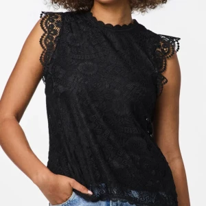 Svart spetsblus från Pieces - Svart blus i spets från Vero Moda med rund hals och dekorativa spetsdetaljer vid ärmslut och nederkant. Ärmlös modell med snyggt mönstrad spets och liten knapp i nacken. Aldrig använd. 