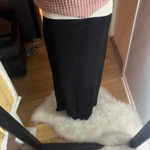 Svart långkjol i mjukt material - Säljer en svart långkjol med rak och enkel siluett. Kjolen är tillverkad i ett mjukt och följsamt material som sitter bekvämt runt midjan. Perfekt för dig som gillar minimalistisk stil och vill ha en kjol som är lätt att matcha med olika toppar.