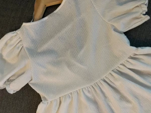 Vit blus med puffärm från Gina Tricot - Supersöt vit blus från Gina Tricot i storlek XS. Blusen har puffiga korta ärmar, omlottkänsla med knyt framtill och volang nedtill. Materialet är lätt strukturerat och känns luftigt, perfekt för varmare dagar. Snygg att styla med jeans eller kjol!