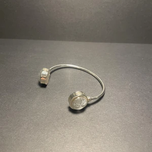 Silverfärgat armband med rundade ändar - Stilrent armband i silverfärg med öppet avslut och två runda, platta ändar. Designen är minimalistisk och modern, med en blank yta som ger en cool vibe. Perfekt för dig som gillar enkla men snygga accessoarer som sticker ut lite extra.