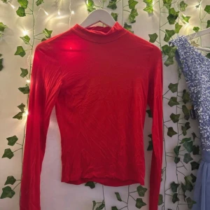 Röd polotopp med långa ärmar - Snygg röd polotopp med lång ärm och tight passform. Enkel och stilren design som passar perfekt till jeans eller kjol. Tunnare material som känns skönt mot huden och ger en clean look.