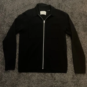 Blå overshirt från Jack and Jones - Stilren svart overshirt från J.Lindeberg med två bröstfickor och hel dragkedja framtill. Skjortan har klassisk krage och lång ärm, perfekt för en clean och modern look.