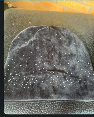 Svart sammetsmössa med glittriga detaljer - Snygg svart mössa i mjuk sammet med glittriga prickar som ger en cool och festlig vibe. Perfekt för dig som vill sticka ut lite extra under höst och vinter. Mössan har en enkel form och passar de flesta stilar.