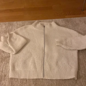 Vit ribbad kofta med dragkedja - Säljer en vit ribbstickad kofta med dragkedja framtill och hög krage. Tröjan har långärmade ärmar och är tillverkad i ett mjukt stickat material som känns riktigt skönt. Perfekt för dig som gillar en clean och chill stil.