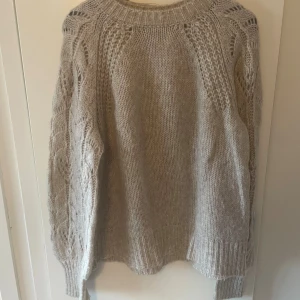 Beige stickad tröja från Kappahl - Säljer en beige stickad tröja från Kappahl i storlek M. Tröjan har snygga långärmade ärmar med mönstrad stickning och ribbade muddar vid hals, ärmslut och nederkant. Perfekt för dig som gillar mysiga och stilrena plagg med lite extra detaljer.