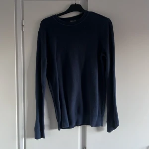 Mörkblå stickad tröja dressman - En stilren mörkblå stickad tröja med rund halsringning och långa ärmar. Tröjan har en enkel och klassisk design som passar perfekt till jeans eller chinos. Materialet är mjukt och ger en skön känsla hela dagen dressman