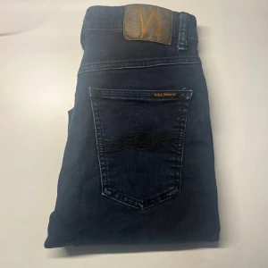 Nudie Jeans - Snygga mörkblå jeans från Nudie Jeans i slim fit. Klassisk femficksmodell med guldfärgade detaljer och Nudie-logga på bakfickan. Jeansen har hög midja och är tillverkade i stretchigt denim för en bekväm passform. Modellapp saknas. Midja 34cm, längd 99cm.  Ifall det inte finns någon bild i annonsen där jag bär plaggen jag säljer så är det för att jag ej kan ha storleken heller passformen, så kolla måtten för storlek och googla på modellnamnet för passform 😉 s3