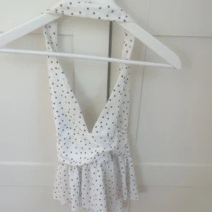 Vit prickig topp med volang - Supersöt vit tooo med svarta prickar och volangkant nedtill. Djup v-ringning och breda axelband.