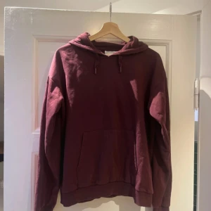 Vinröd hoodie med huva och ficka - Säljer en vinröd hoodie med huva och snörning. Tröjan har en stor magficka framtill och långa ärmar med muddar. Perfekt för chill dagar och enkel att matcha med jeans eller mjukisbyxor.