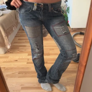 Patchade blå jeans med slitningar -  Säljer ett par blå jeans med coola patchade detaljer och slitningar på både fram- och baksida.  Sååå unik och cool🤩🤩 de är väldigt lågmidjade och skulle säga att de är mindre bootcut/straight. Är 168 och bär S  