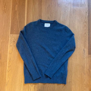 Blå stickad tröja These Glory Days - Mysig blå stickad tröja från These Glory Days i storlek M. Tröjan har rund hals, långa ärmar och ribbade muddar vid hals, ärmslut och nederkant. Perfekt för dig som gillar enkel och stilren design med skandinavisk känsla.