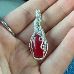 Handgjord silverberlock med röd sten - Unikt halsband med en droppformad röd sten infattad i intrikat virad silvertråd. Hängsmycket har snygga snirkliga detaljer och en blank, djup röd färg som verkligen poppar. Perfekt för dig som gillar statement-smycken med konstnärlig känsla.