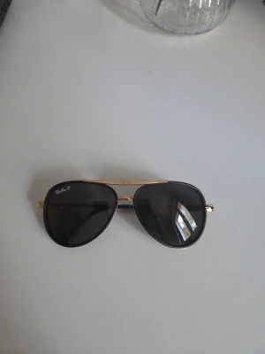 Ray-Ban aviator solglasögon guld/svart - Snygga Ray-Ban aviator solglasögon med guldfärgade metallbågar och svarta polariserade linser. Klassisk pilotform med tunna, mönstrade skalmar och svarta detaljer vid ändarna. Perfekt för dig som vill ha en tidlös och cool look.bra qulitet öckså