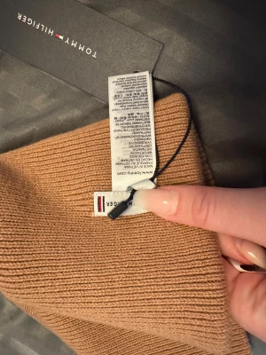 Beige ribbad mössa Tommy Hilfiger - Snygg beige ribbstickad mössa från Tommy Hilfiger med klassisk logga framtill. Mjuk och skön passform, perfekt för kyliga dagar. Materialet är stickad bomull och polyester, vilket gör den både varm och stilren.