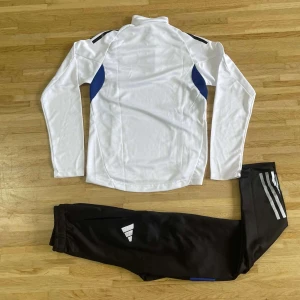 Svarta Adidas träningsbyxor - Svarta träningsbyxor från Adidas med vita ränder längs benet och logga på låret. Byxorna har elastisk midja och är gjorda i ett mjukt syntetmaterial som passar perfekt för sport och träning.