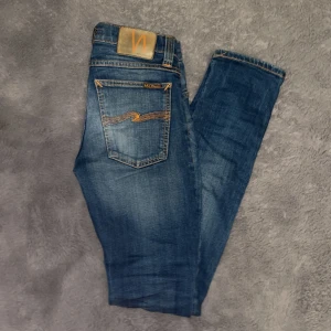 Blå Nudie Jeans Slim W26 L32 - Snygga blå jeans från Nudie Jeans med klassisk orange söm på bakfickorna och läderpatch i midjan. Jeansen är i super bra skick och i storlek w26 l32 och det passar runt 160 eller längre‼️Hör av dig direkt vid frågor eller funderingar!😁